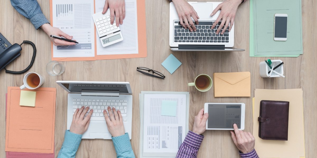 Bird's eye view of people working on their laptops with colourful notebooks next to them.