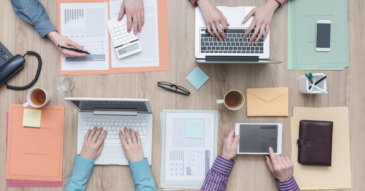 Bird's eye view of people working on their laptops with colourful notebooks next to them.